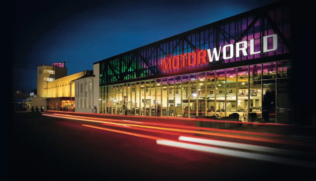 Illuminated glass facade of Motorworld at night with light trails on the street, Böblingen