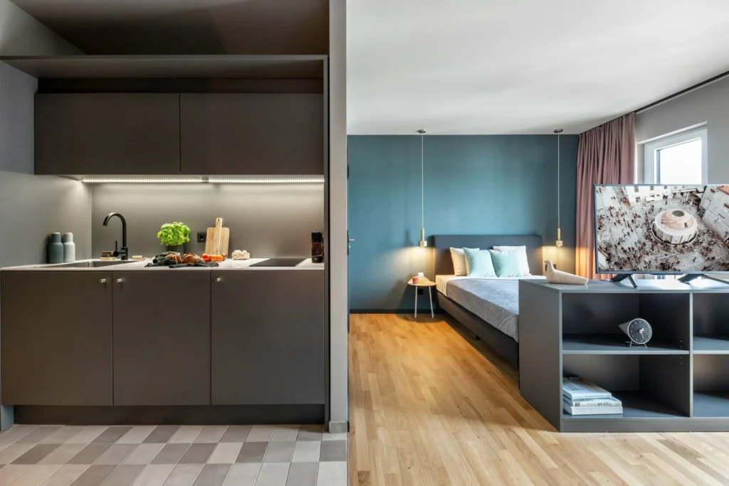 Kitchenette and bed with TV on a shelf in front of a blue wall in Apartment M, apartment Braunschweig