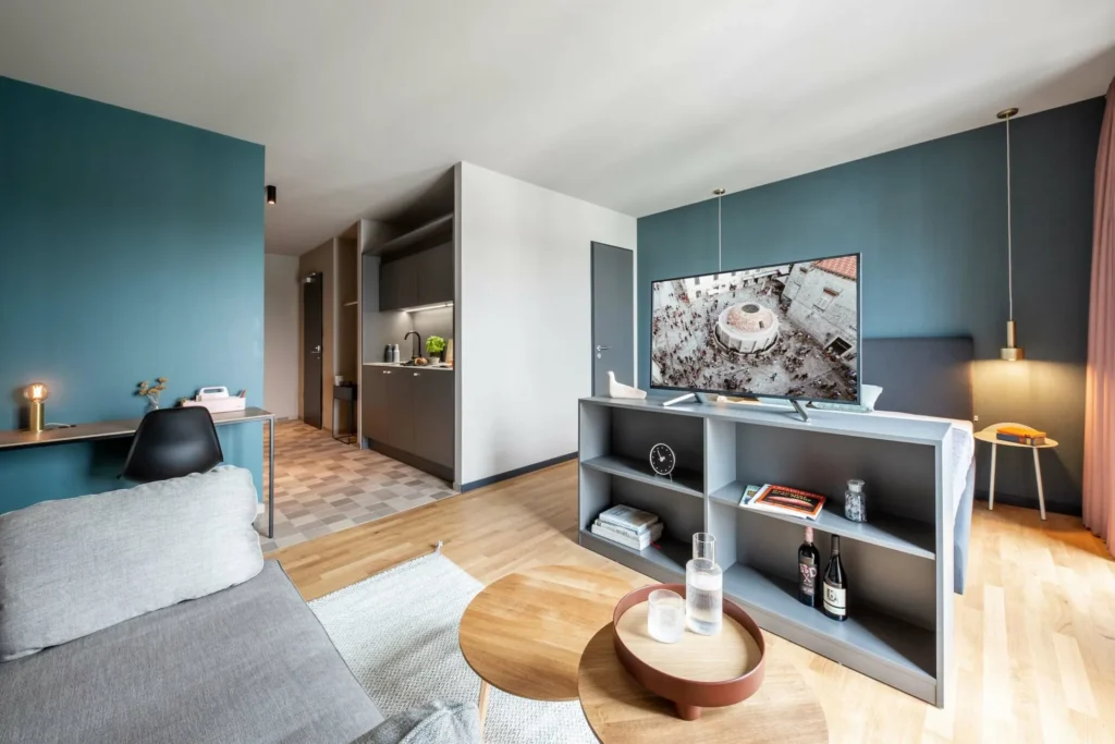 Overview with bed, shelf as a divider, coffee table, work area and kitchen in Apartment M, ipartment Braunschweig