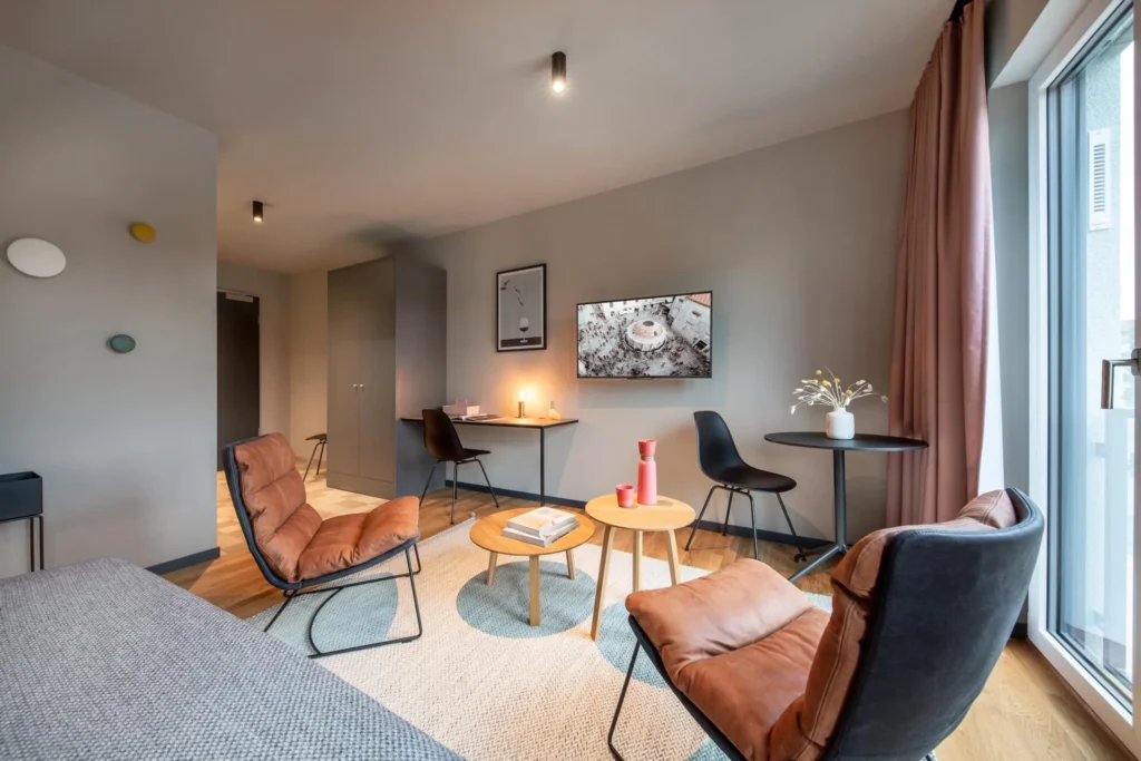 Sitting area with armchairs, coffee tables and dining table by the window in Apartment S, Braunschweig