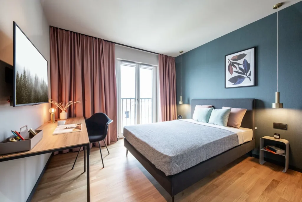 Schlafbereich mit Doppelbett, Schreibtisch und bodentiefem Fenster im Apartment XS, ipartment Braunschweig
