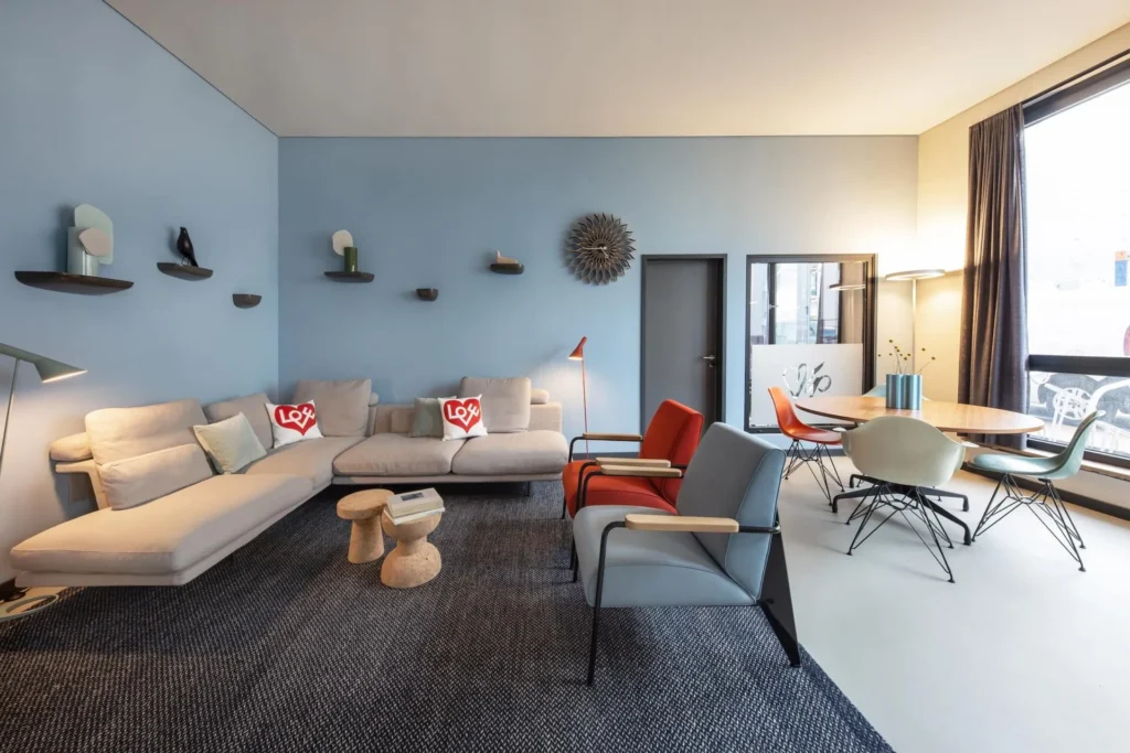 Vitra lounge with sofa, chairs and dining table in front of a light blue wall, ipartment Braunschweig