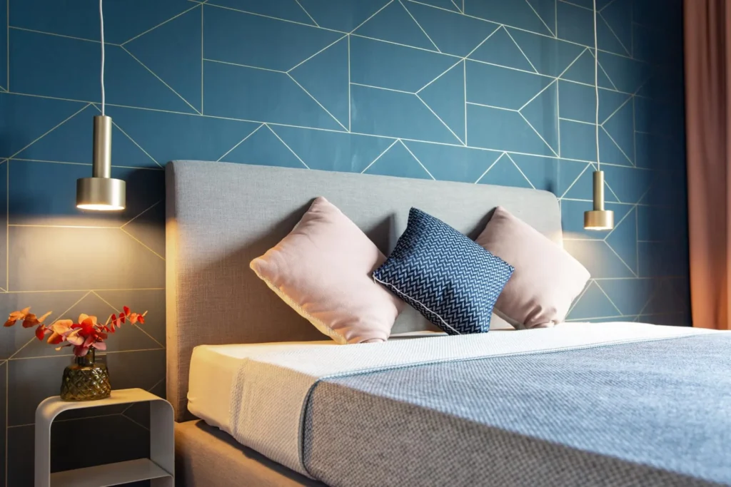 Double bed with pillows in front of a blue patterned wallpaper and brass pendant lights in the Luxury apartment, ipartment Darmstadt