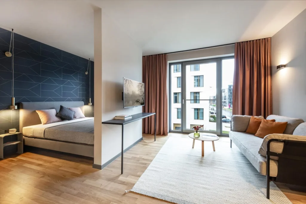 Living and sleeping area with double bed, sofa and floor-to-ceiling window in the Medium apartment, ipartment Darmstadt