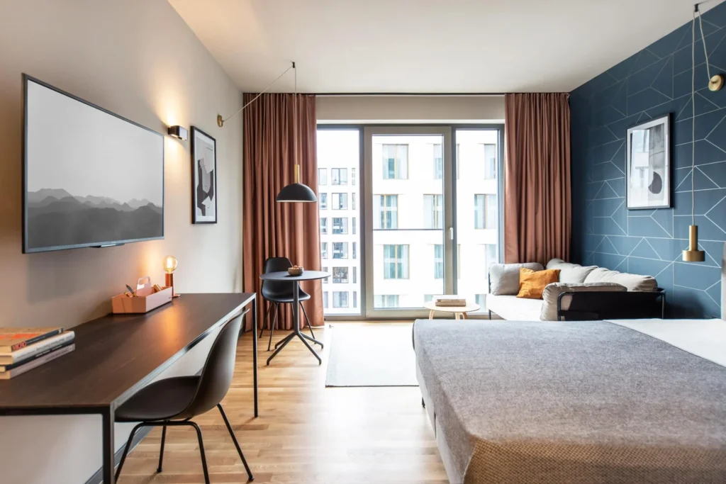 Wohnbereich mit Schreibtisch, Esstisch, Sofa und Bett vor blauer Mustertapete im Apartment Smart, ipartment Darmstadt