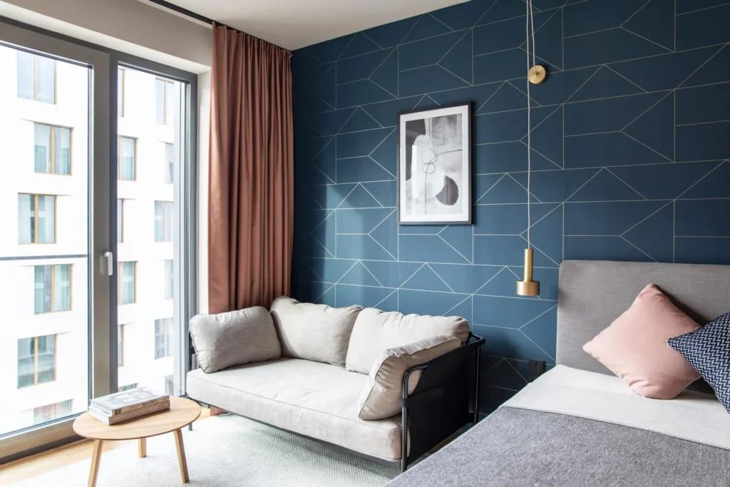Sofa and bed in front of a blue patterned wallpaper with a brass pendant light in the Smart apartment, ipartment Darmstadt