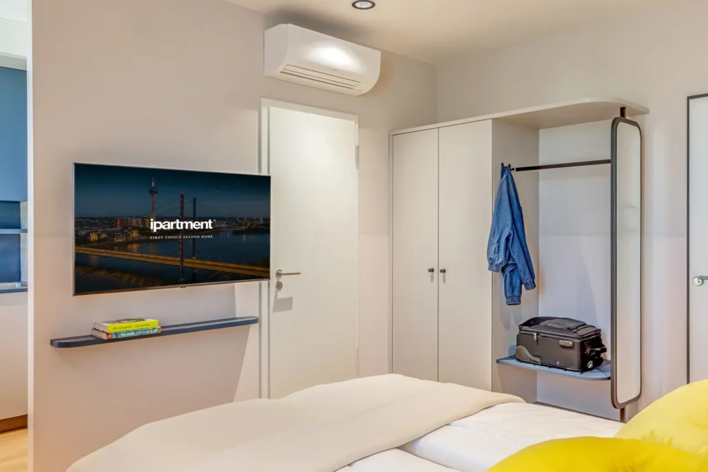 Sleeping area with wardrobe, air conditioning, smart TV on the wall and suitcases in the shelf, ipartment Düsseldorf
