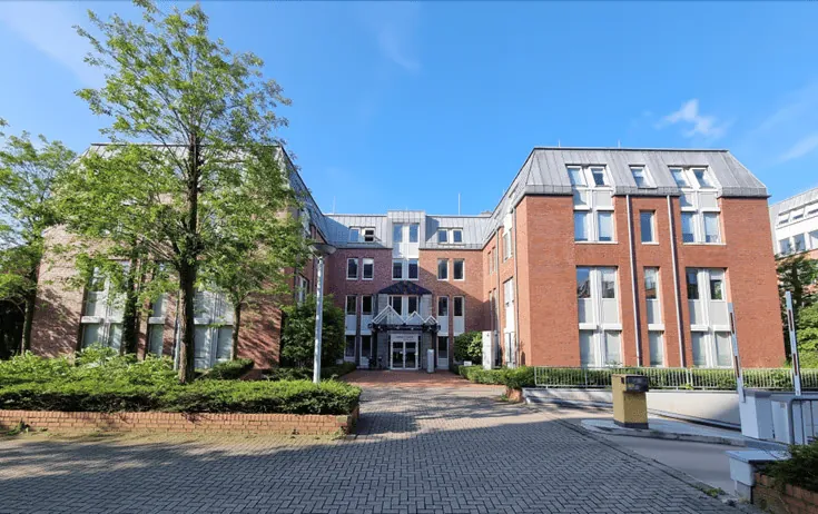 Frontansicht des Backsteingebäudes an der Hansaallee mit Eingang, Bäumen und Pflasterfläche davor