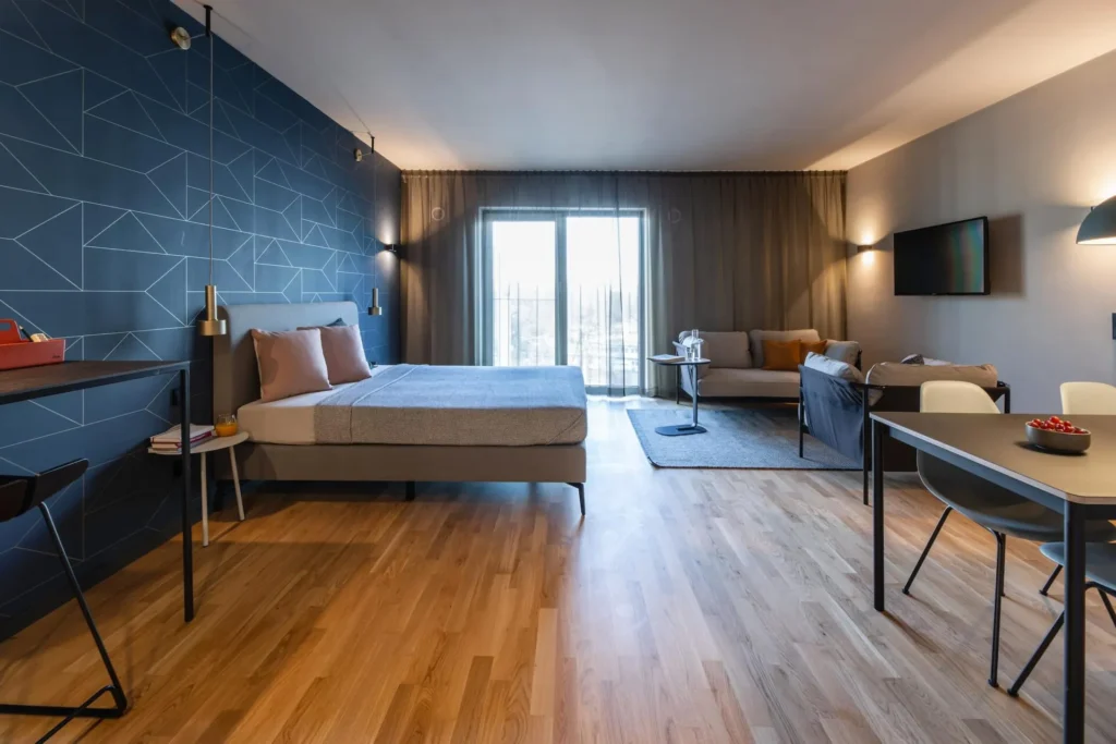 Großzügiger Wohnraum mit Bett, Sofa und Essplatz vor der Balkontür im Apartment L, ipartment Frankfurt Airport