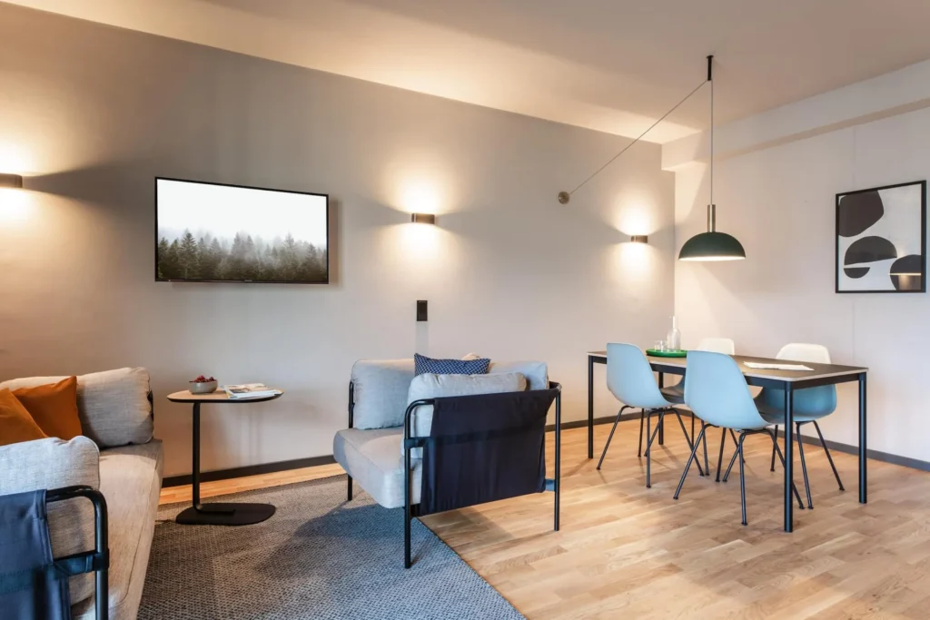 Sitting area with dining area, armchair and TV on the wall in Apartment L, ipartment Frankfurt Airport