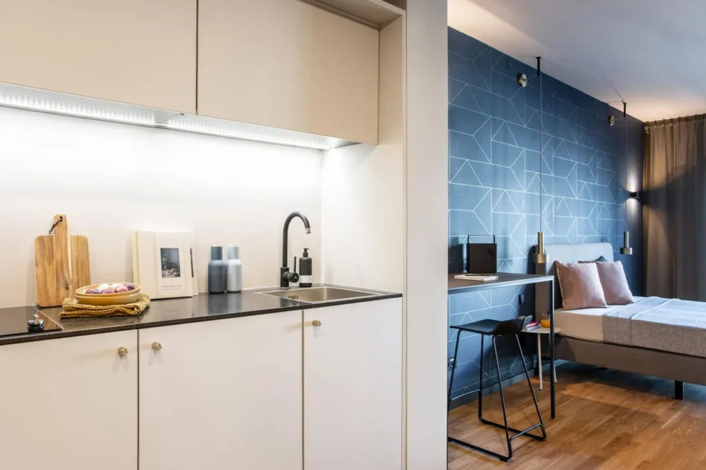 Kitchen area and bed in the L apartment, ipartment Frankfurt Airport, with a blue wallpaper wall