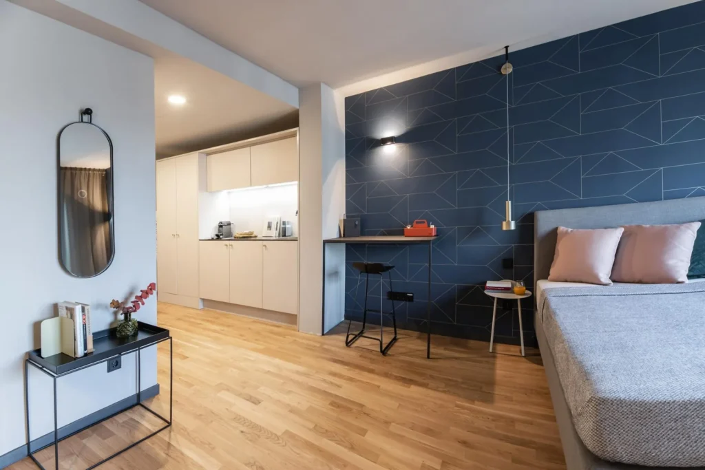 Bed, desk and kitchenette with wall mirror in Apartment L, ipartment Frankfurt Airport