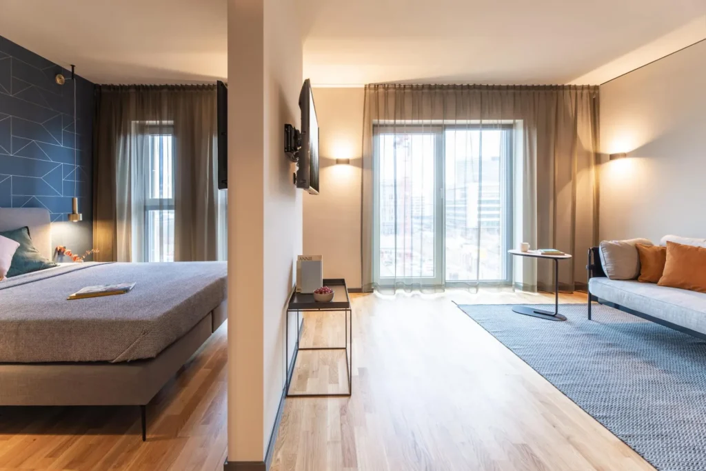 Sleeping area with double bed and sofa in front of floor-to-ceiling window in Apartment M, apartment Frankfurt Airport