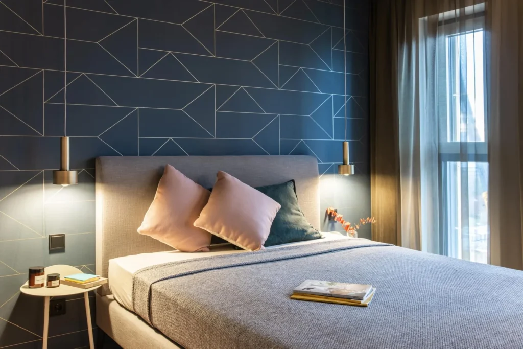 Double bed with pillows in front of a dark wall with a striped pattern in Apartment M, ipartment Frankfurt Airport