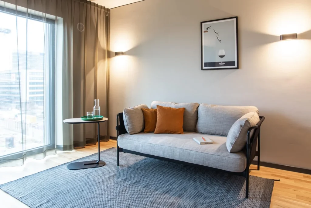 Sofa with cushions and carpet in front of a large window in the living area of the M apartment, ipartment Frankfurt Airport