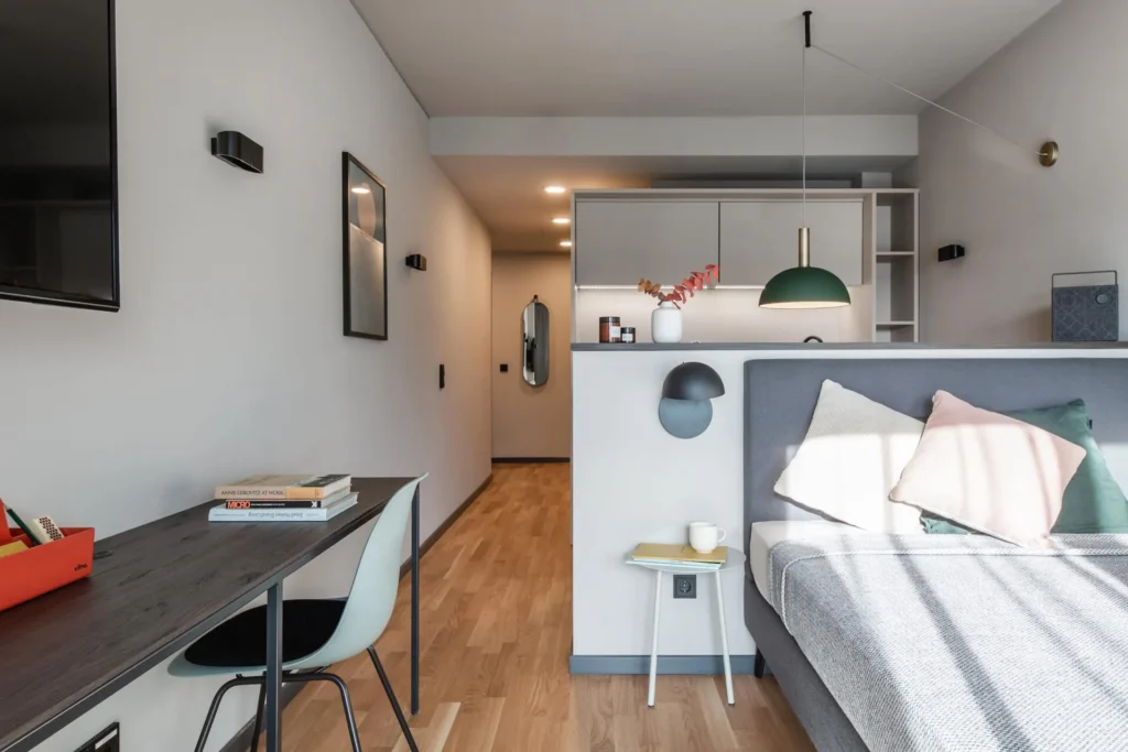 Sleeping area with box spring bed, desk and kitchenette in the XS apartment, ipartment Frankfurt Airport