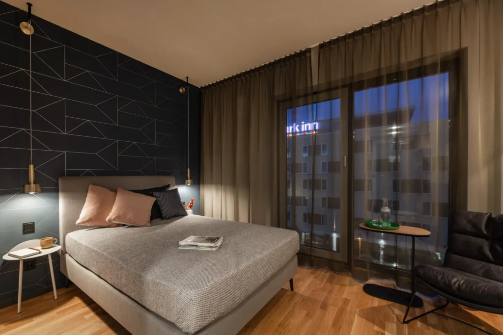 Boxspring bed in front of a dark wall with a graphic pattern and a balcony door in the XS apartment, ipartment Frankfurt Airport