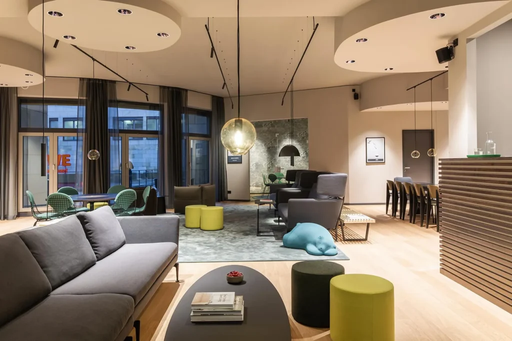 Vitra lounge with grey sofa, coffee table and stools; on the right is a long wooden table, ipartment Frankfurt Airport