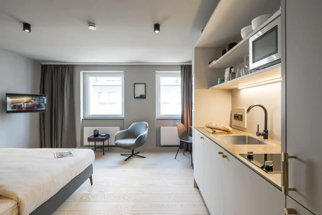 Living and sleeping area with kitchenette, armchair and two windows in the Xtra Smart apartment, ipartment Frankfurt Bahnhofsviertel