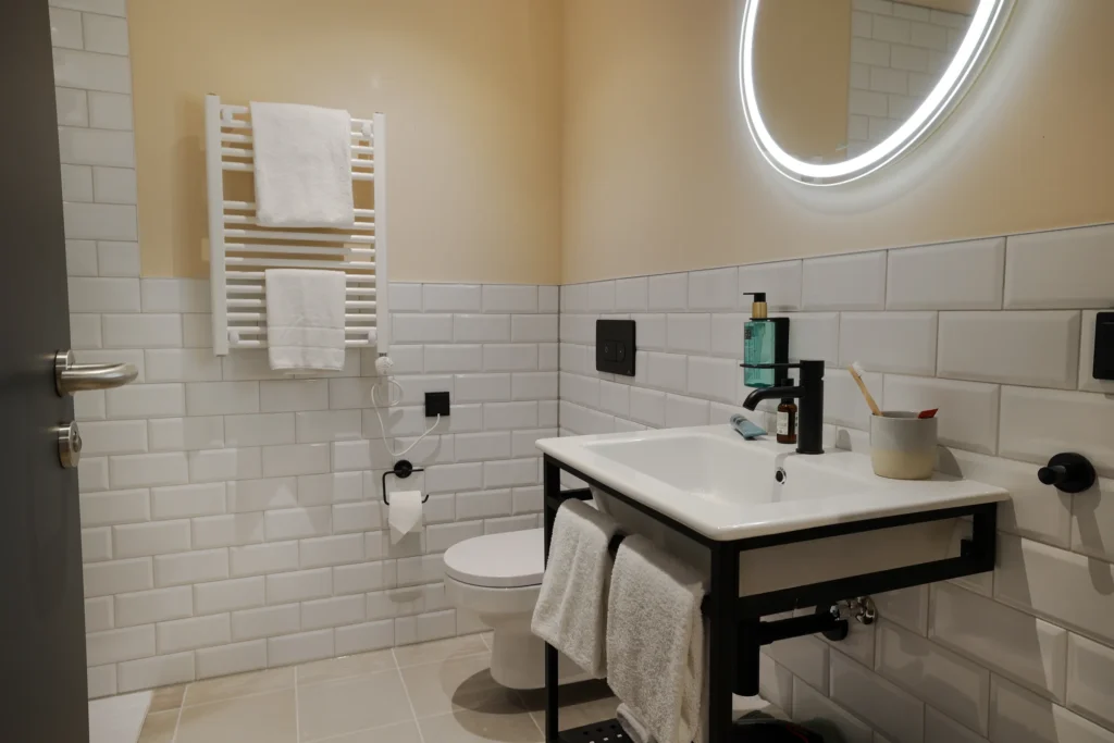 Bathroom with sink, round mirror with light, toilet and towel heater, ipartment Frankfurt Eastside