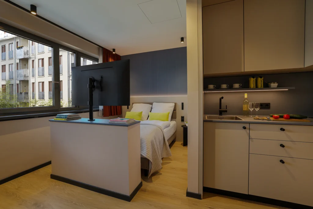 Apartment with work area at the counter, double bed with yellow pillows and kitchenette, ipartment Frankfurt Eastside