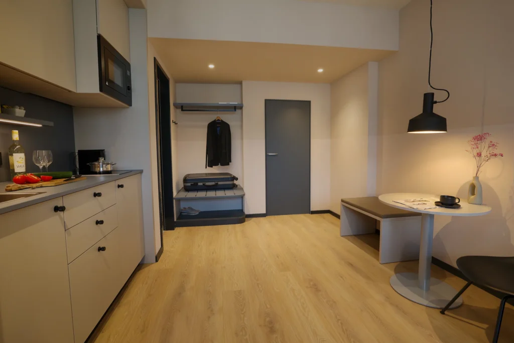 Kitchen area on the left, wardrobe with suitcases and dining table to the right under a pendant light, ipartment Frankfurt Eastside