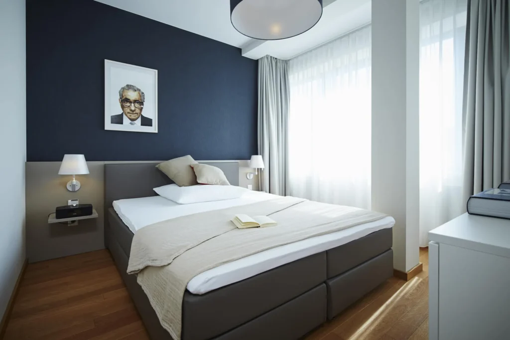 Sleeping area with box spring bed, dark blue walls and floor-to-ceiling windows in Apartment L, ipartment Frankfurt Europaviertel