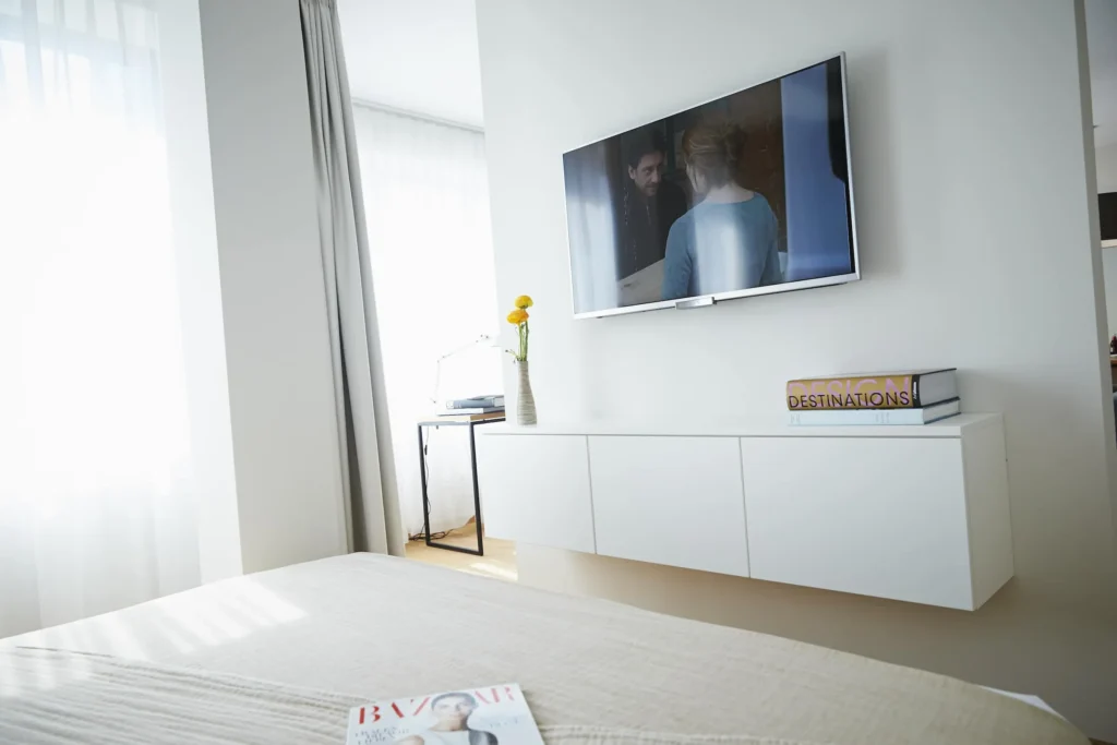 Wall-mounted TV over a white sideboard; in the foreground is the bed in apartment L, Frankfurt Europaviertel