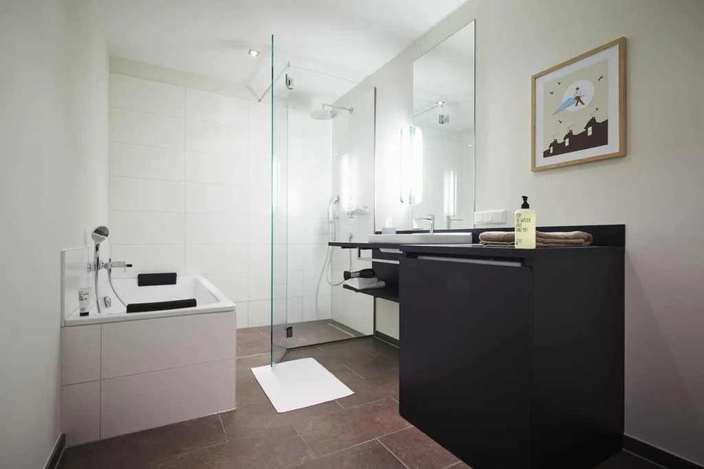 Bathroom with bathtub, glass shower and sink with black cabinet in apartment L, ipartment Frankfurt Europaviertel