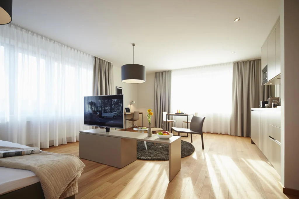 Wohnbereich mit Fernseher, Couchtisch, Küchenzeile und großen Fenstern im Apartment M, ipartment Frankfurt Europaviertel