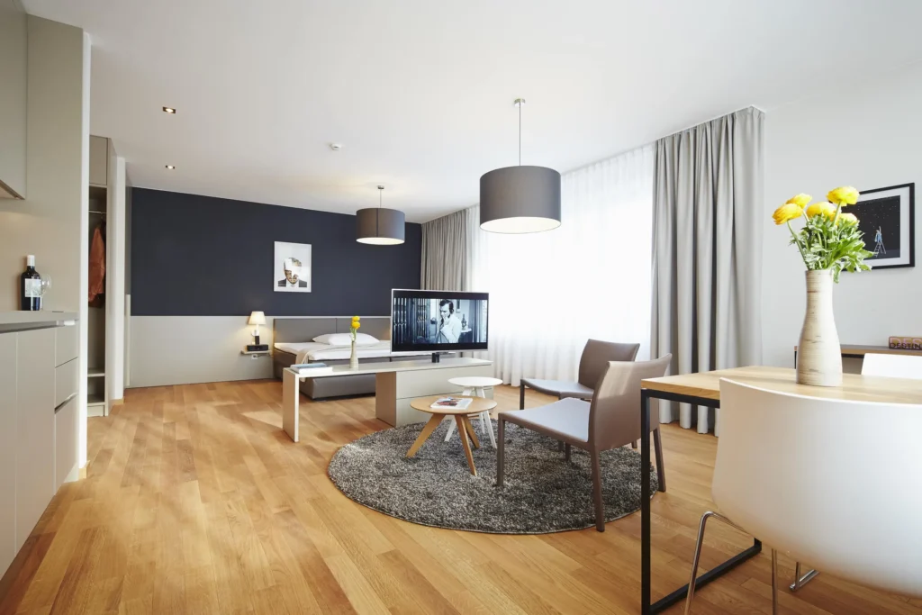 Spacious living and sleeping area with seating group, dining area and dark blue wall in apartment M, ipartment Frankfurt Europaviertel