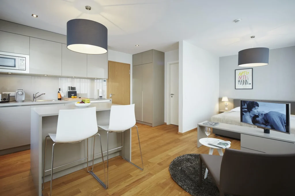 Kitchen with breakfast table and bar stools, behind it is a bed and TV in apartment S, apartment Frankfurt Europaviertel