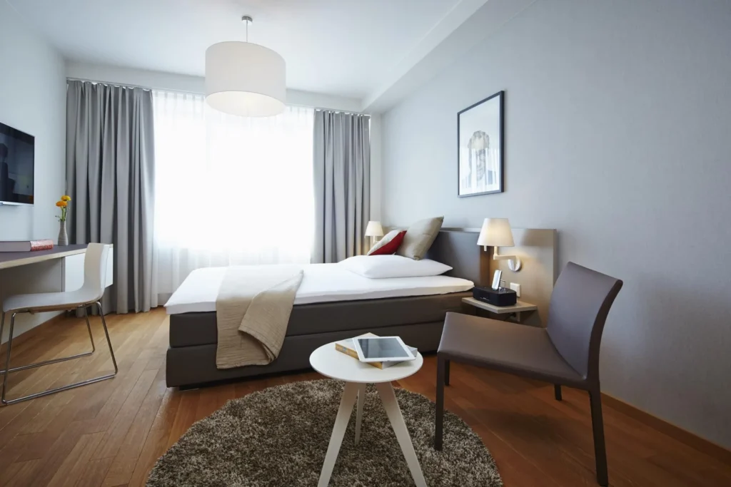 Sleeping area with box spring bed, armchair, carpet and floor-to-ceiling window in Apartment S, ipartment Frankfurt Europaviertel