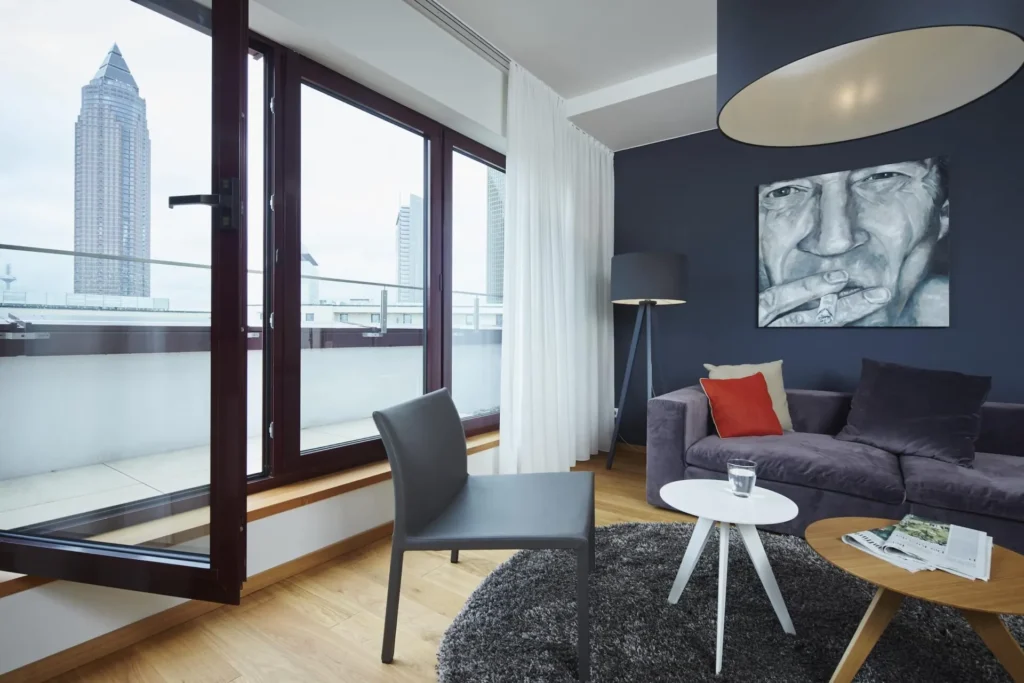 Armchair and sofa on the open balcony window overlooking Frankfurt high-rise buildings in the XL apartment, ipartment Frankfurt Europaviertel