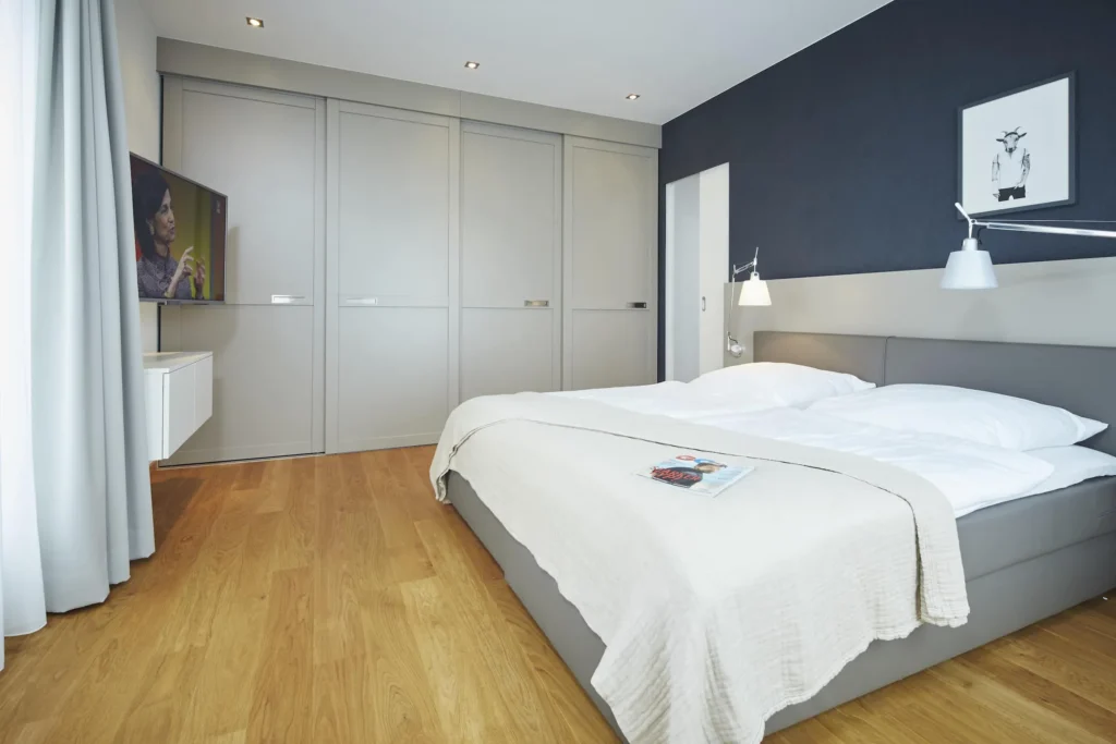 Bedroom with double bed, dark blue wall and large built-in wardrobe in the XL apartment, ipartment Frankfurt Europaviertel