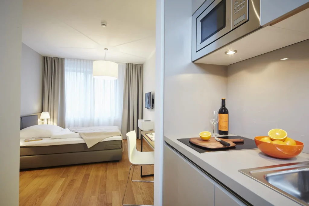 Sleeping area with a bed by the window and a kitchenette with a microwave in the XS apartment, ipartment Frankfurt Europaviertel
