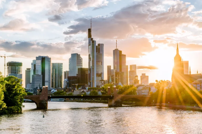 High-rise buildings of the Frankfurt skyline in the backlight of the sun, river with bridge in front of it, Frankfurt am Main
