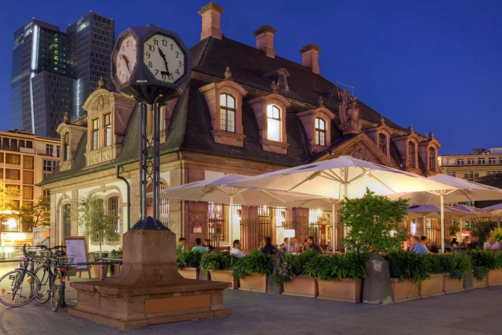Die Hauptwache in Frankfurt am Abend mit Uhr, Terrassenschirmen und Hochhäusern im Hintergrund