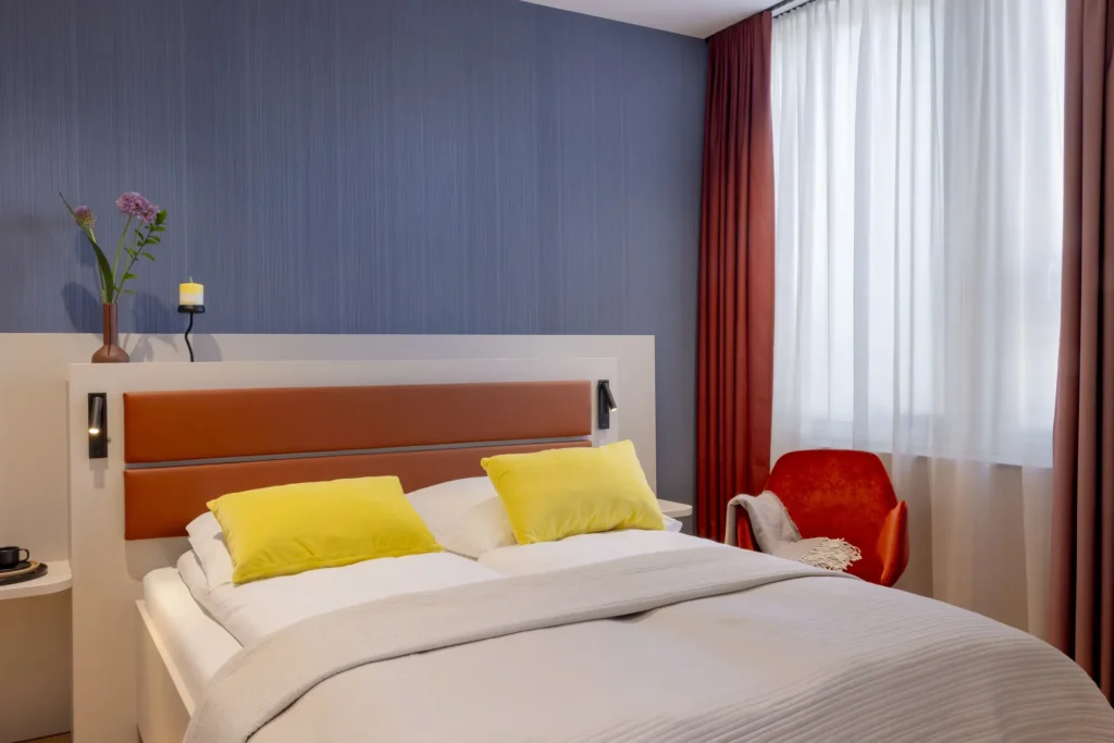 Beispielbild: Schlafbereich mit Doppelbett, gelben Kissen und rotem Sessel am Fenster, Platzhalter für ipartment Fürth