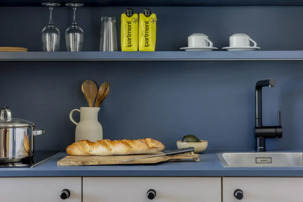 Example image: Kitchen shelf with glasses, cups and beverage cartons above a work surface with baguettes, placeholders for ipartment Fürth