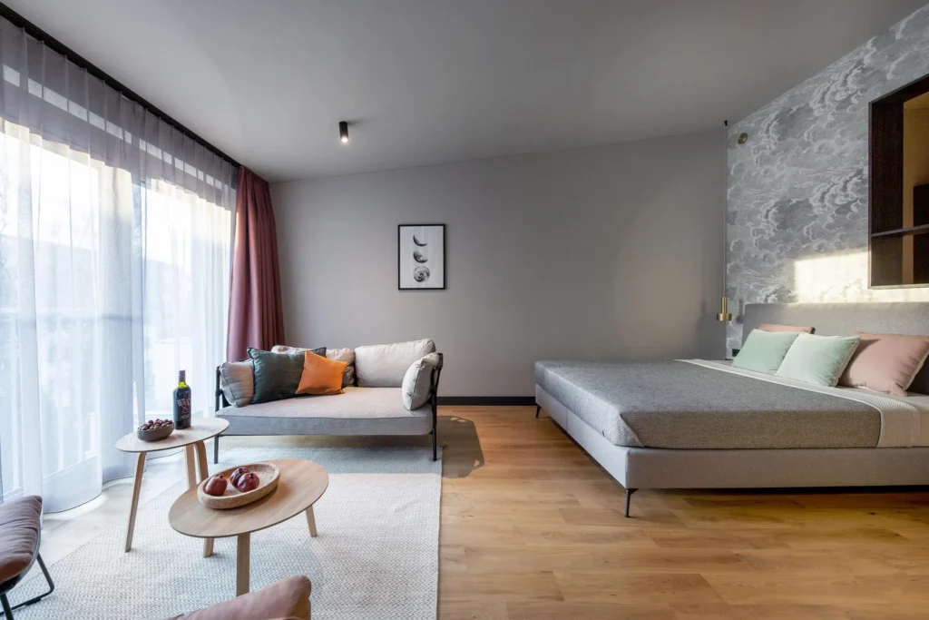 Bed, sofa and coffee tables in front of a floor-to-ceiling window with a curtain in the Medium apartment, ipartment Hamburg Eimsbüttel
