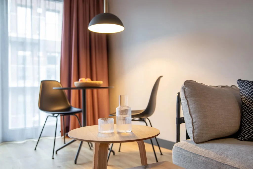 Round wooden table with a carafe, dining table and pendant light by the window in the Medium apartment, ipartment Hamburg Eimsbüttel
