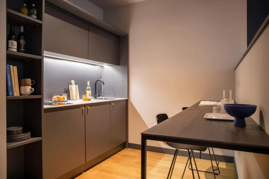 Grey kitchen corner with shelves and a high dining table with bar stools in the Smart apartment, ipartment Hamburg Eimsbüttel