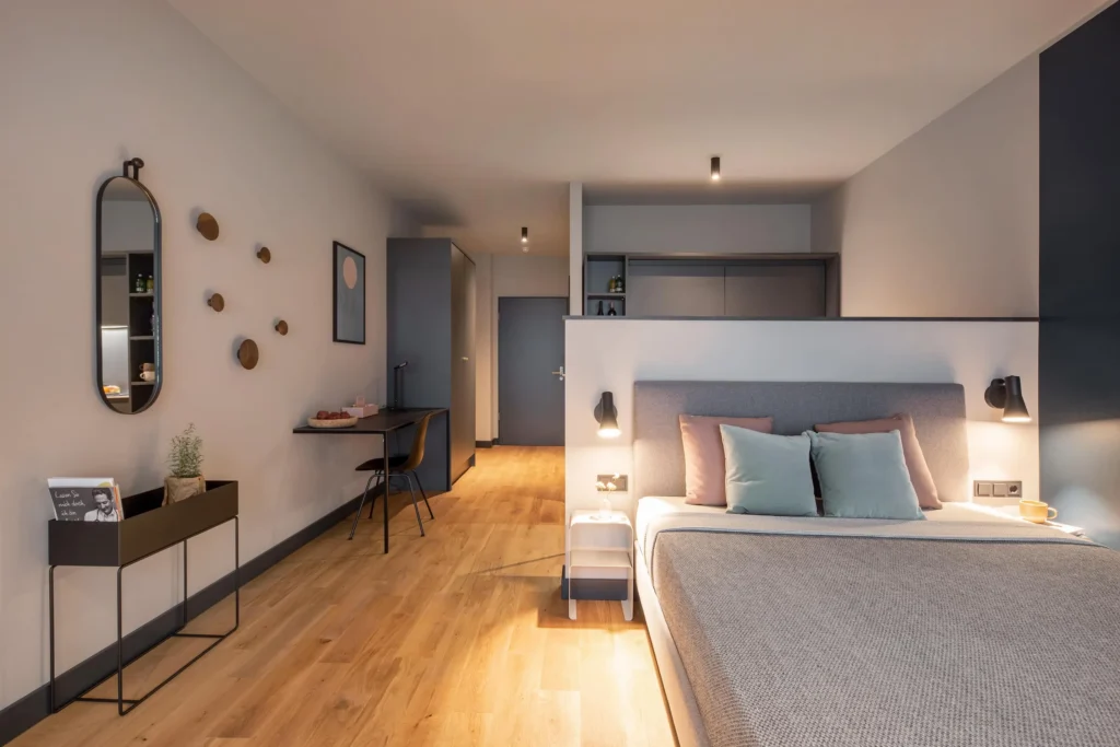 Spacious room with bed, work area, mirror and oak parquet in the Smart apartment, ipartment Hamburg Eimsbüttel