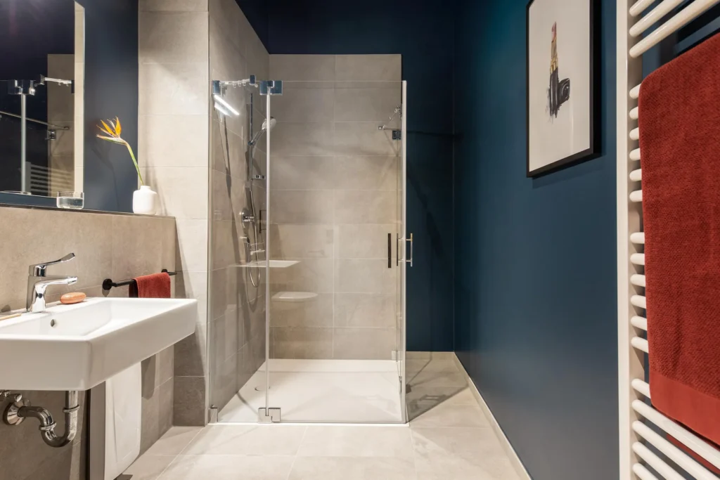 Bathroom with floor-to-ceiling glass shower, sink and red towel on a blue wall, ipartment Hamburg Eimsbüttel