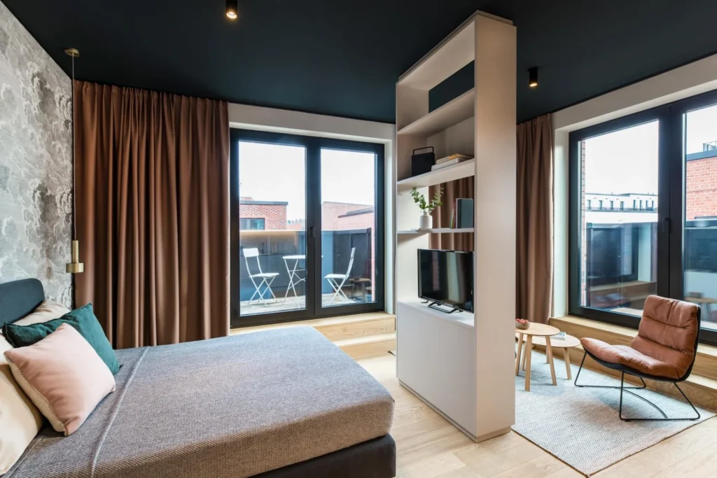 Living and sleeping area with shelving wall, armchair and balcony windows in Apartment M, ipartment Hamburg HafenCity