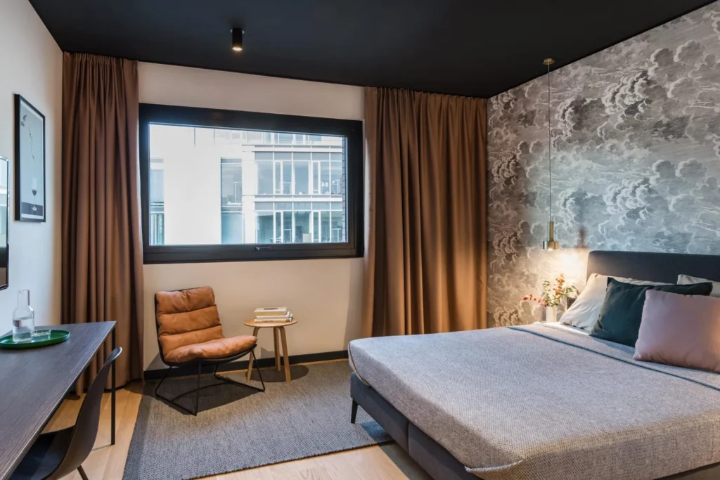Double bed, armchair and desk in front of a wall mural in Apartment S, ipartment Hamburg HafenCity