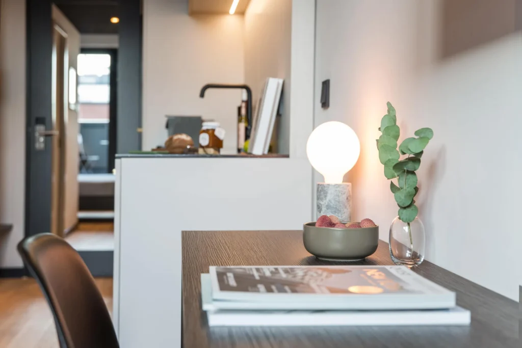 Desk with lamp and magazines in front of the kitchenette in Apartment S, ipartment Hamburg HafenCity