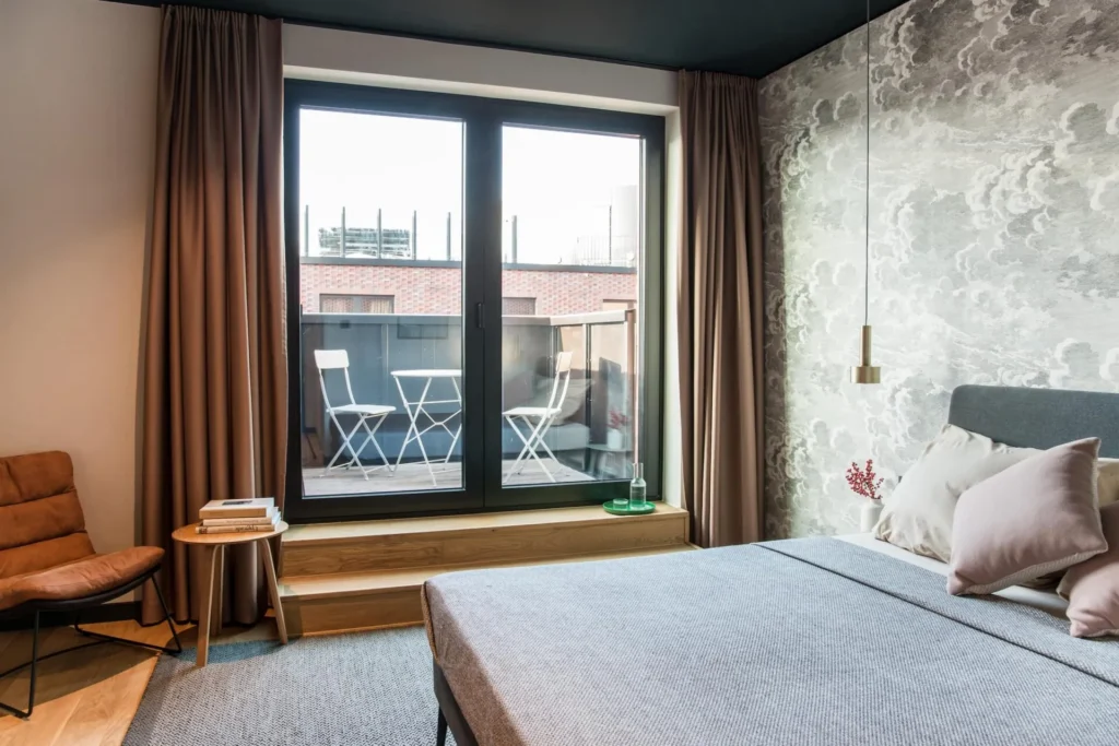 Sleeping area with double bed, armchair and floor-to-ceiling window to the balcony in the XS apartment, ipartment Hamburg HafenCity