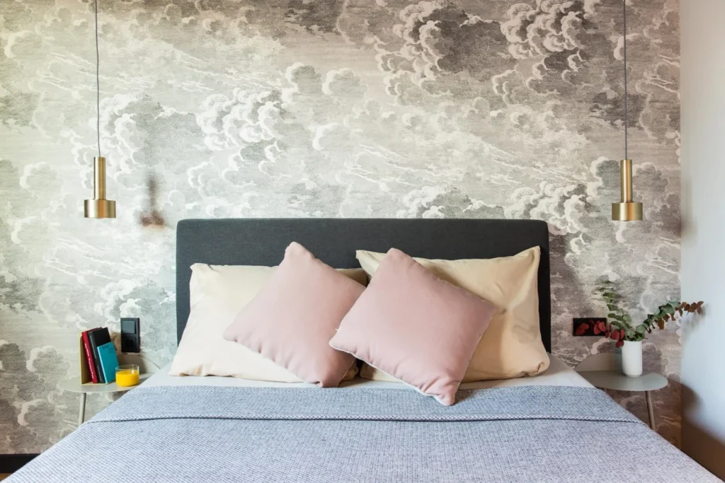 Bed with pillows in front of the cloud wallpaper and pendant lights in the XS apartment, ipartment Hamburg HafenCity